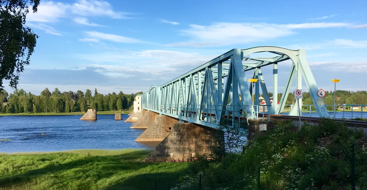 The railway bridge crossing the Torne River from Haparanda to Tornio, with wooded riverbanks